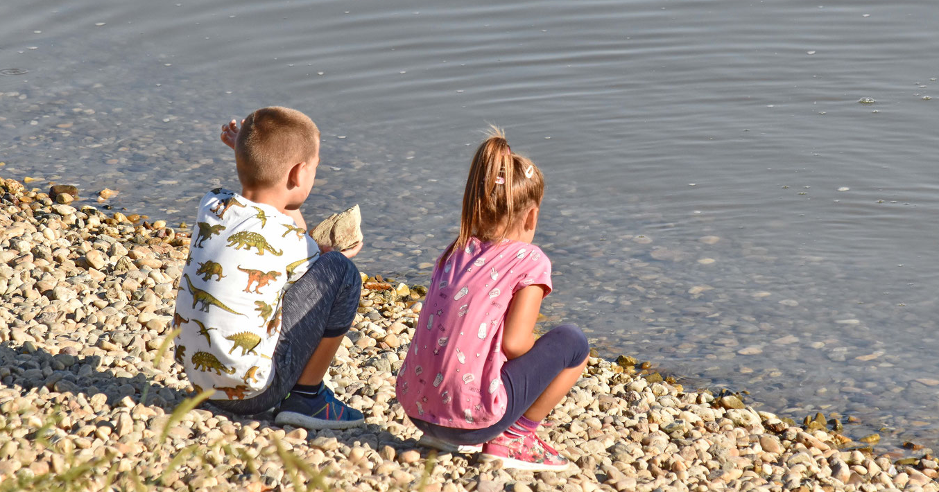 Ein kleiner Junge und ein kleines Mädchen hocken im Sonnenschein am Strand dicht an der Wasserkante.