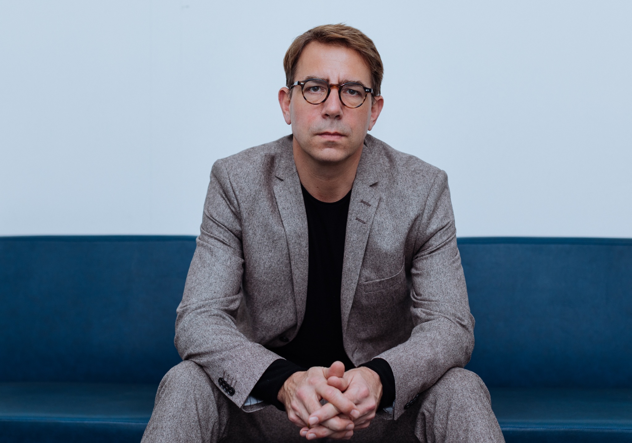 Porträt von Andreas Fischer-Lescano, auf einem Sofa sitzend, die Arme auf die Knie gestützt.
