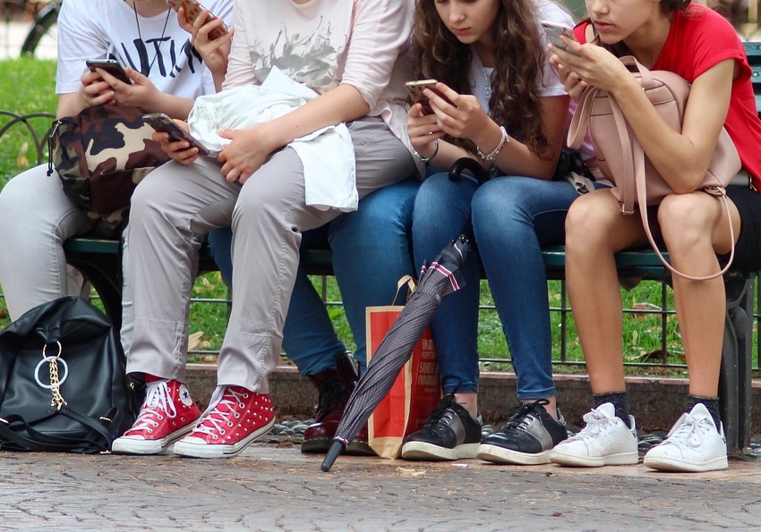 Mehrere Schülerinnen auf einer Bank mit ihren Handys beschäftigt
