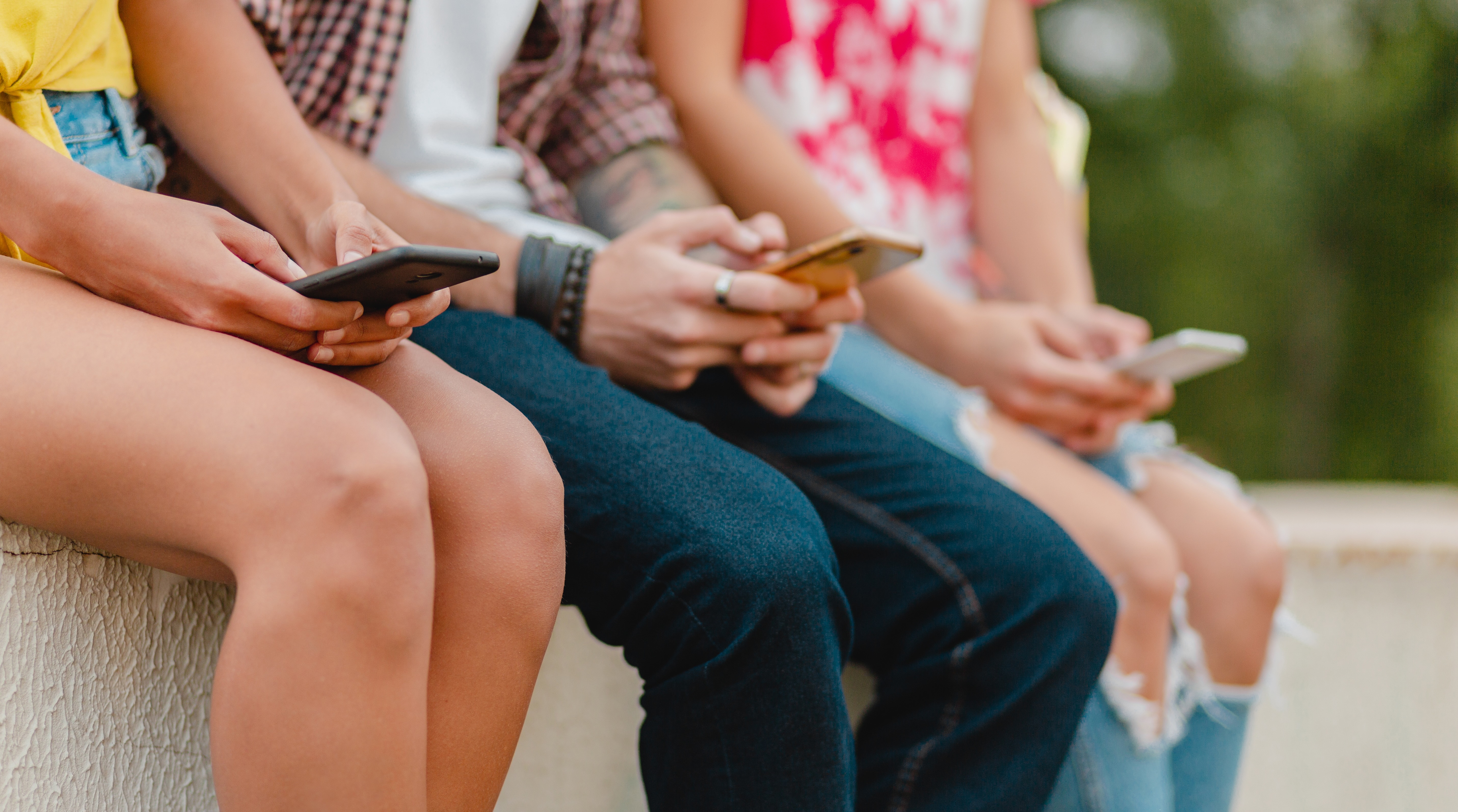 Jugendliche sitzen auf einer Mauer und nutzen ihre Handys.