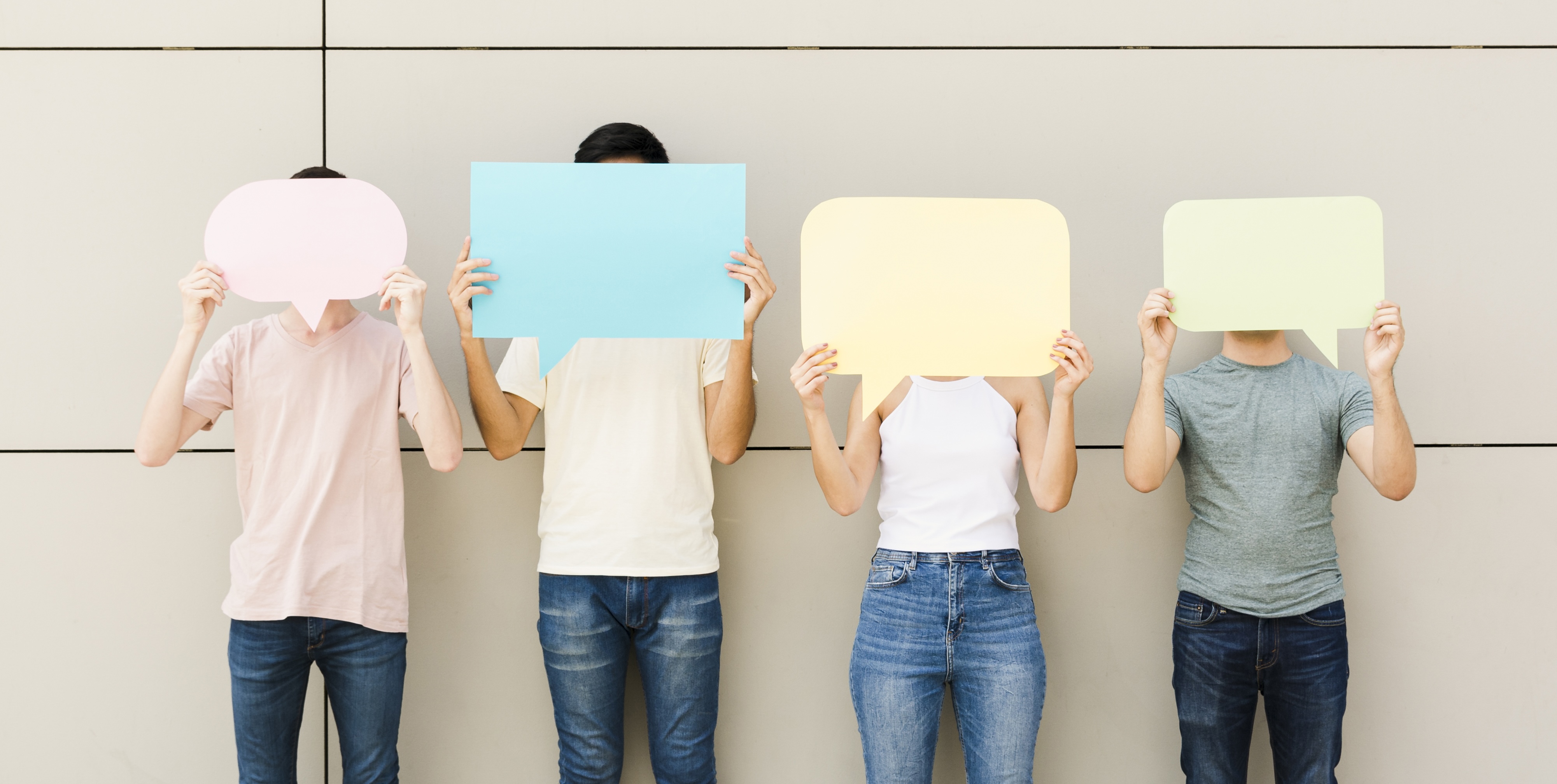 Eine Gruppe von vier jungen Menschen hält sich leere Sprechblasen vor das Gesicht.