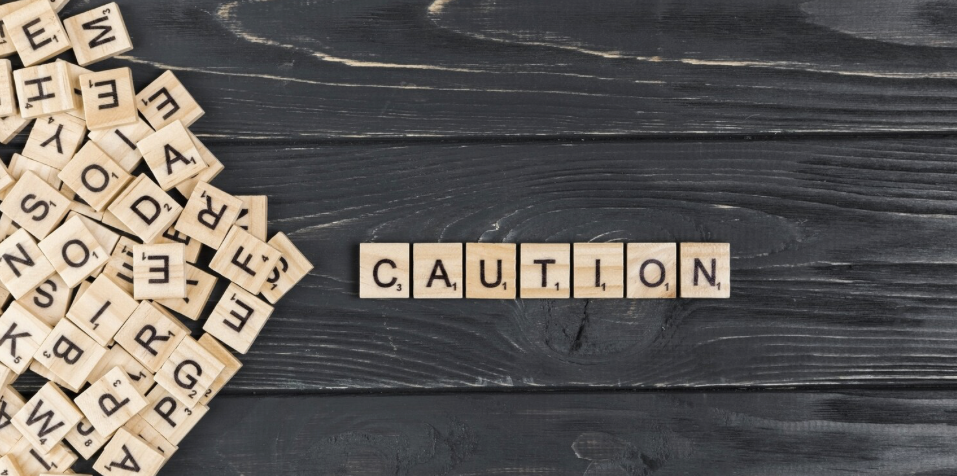 Scrabble-Spielsteine bilden das englische Wort "Caution" auf schwarzem Holz.