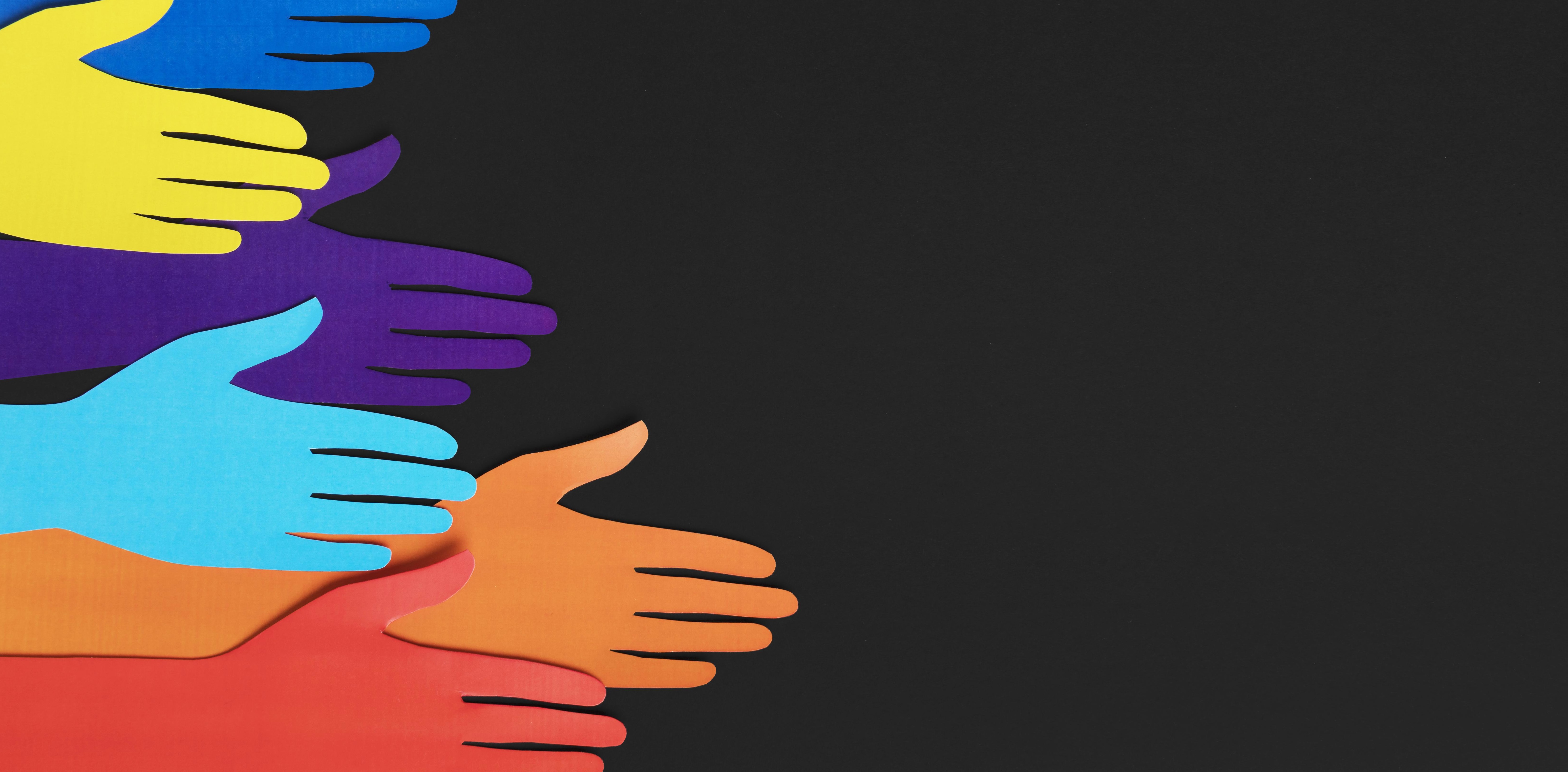 Komposition aus fuenf bunten Haenden aus Papier vor schwarzem Hintergrund.