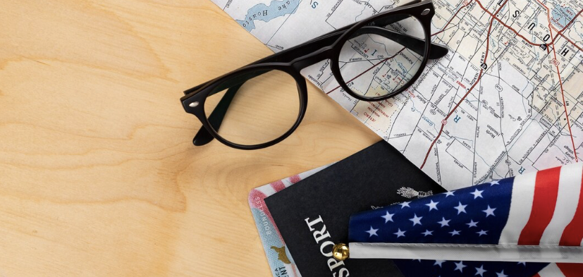 Collage aus Kartenausschnitt USA, Brille, Reisepass, Ausweis und einer kleinen amerikanischen Flagge.