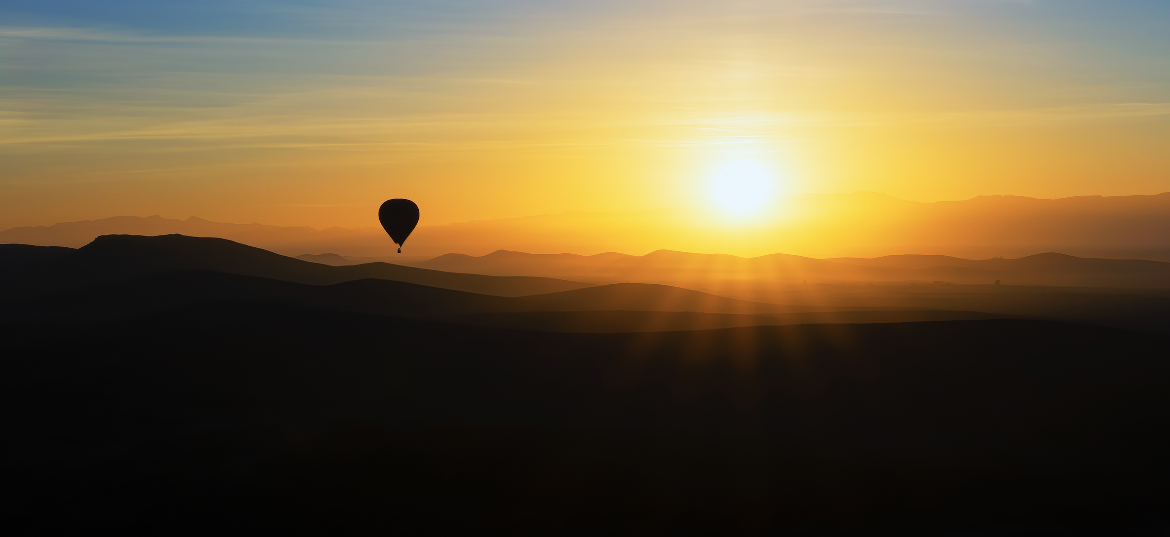 Sonnenaufgang über Hügeln mit Heissluftballon.