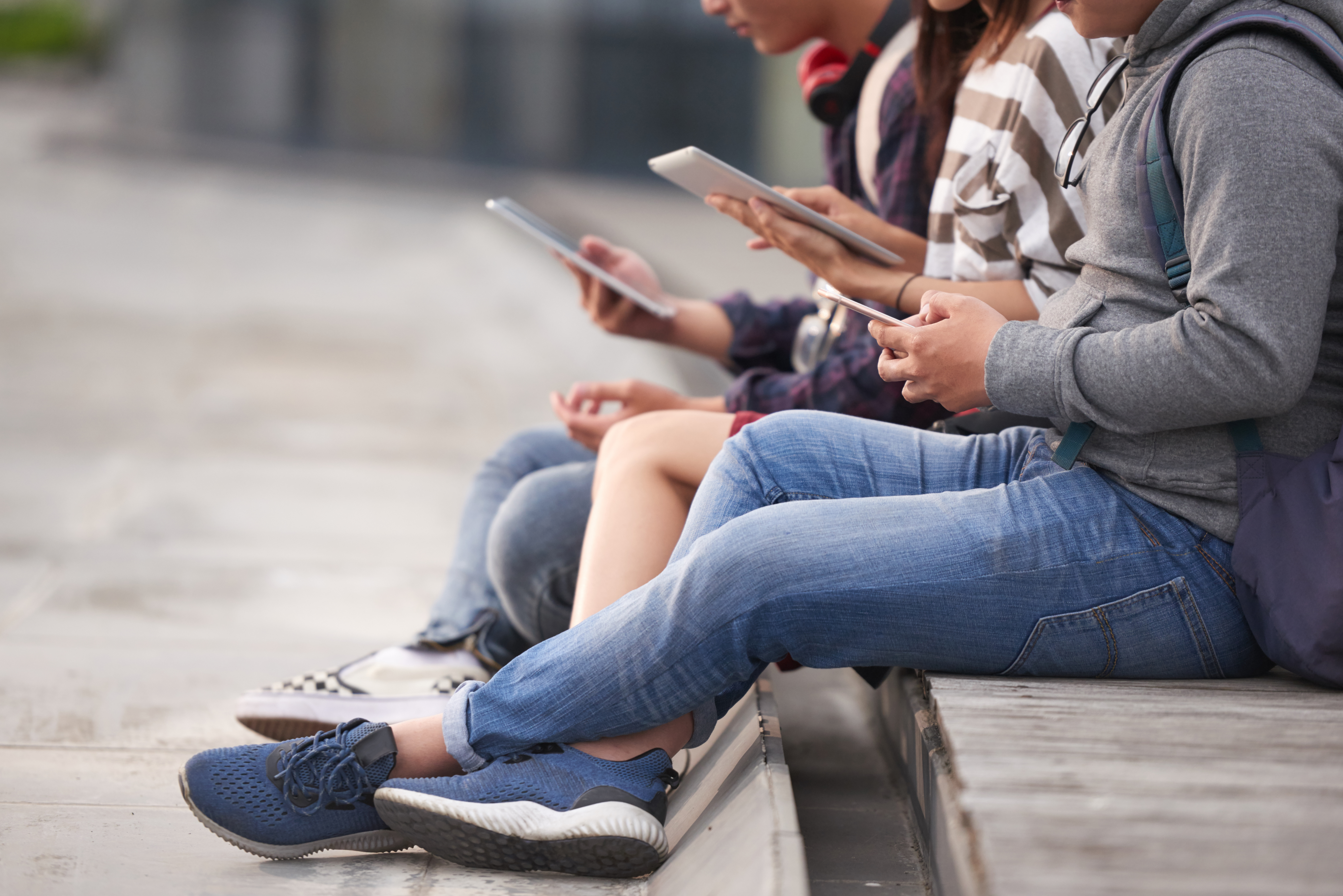 Jugendliche sitzen draussen nebeneinander und nutzen ihre Smartphones.