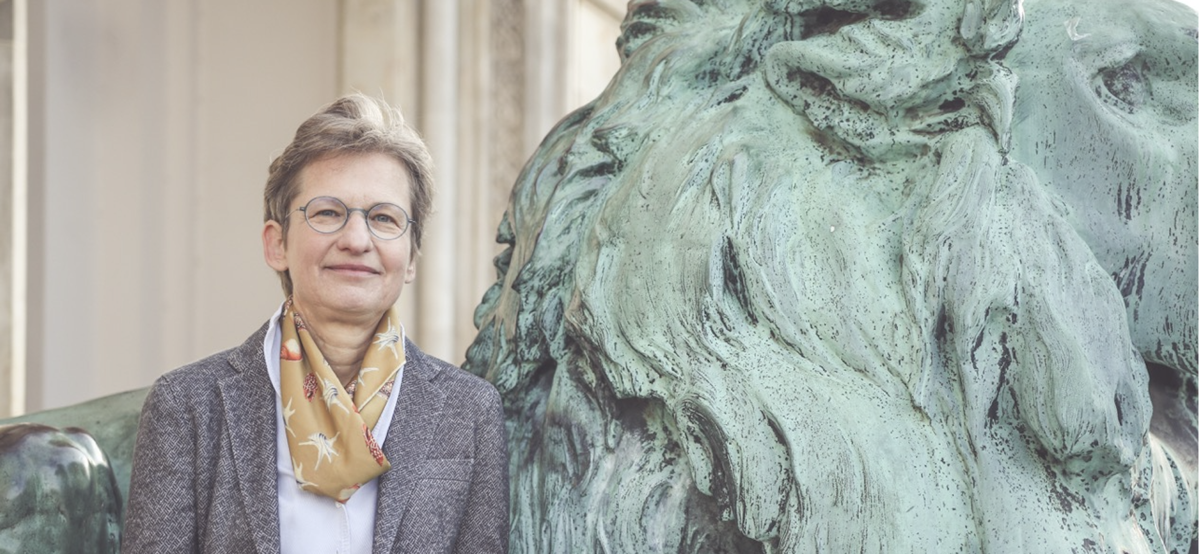 Portraitfoto Eva Barloesius, an steinernen Loewen gelehnt.