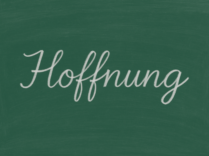 Schultafel, auf der in Schreibschrift mit weisse rKreide das Wort Hoffnung steht.