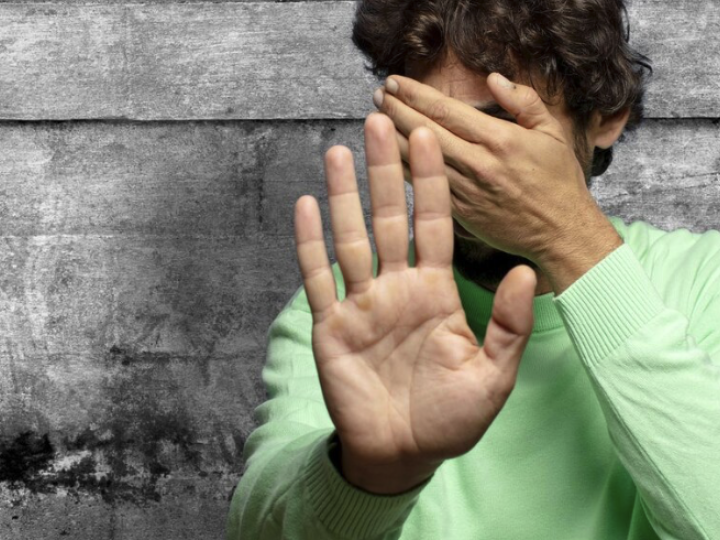 Nahaufnahme eines Jugendlichen vor grauer Wand, der sich schuetzend die Hand vors Gesicht haelt.