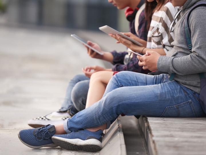 Jugendliche sitzen draussen nebeneinander und nutzen ihre Smartphones.