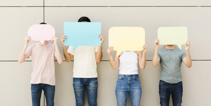 Eine Gruppe von vier jungen Menschen hält sich leere Sprechblasen vor das Gesicht.
