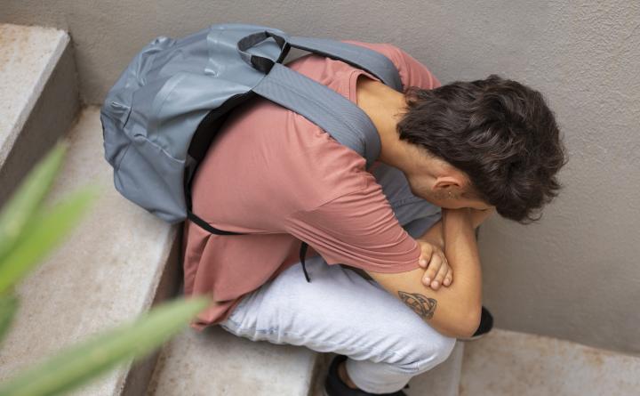 Schueler mit Rucksack sitzt auf einer Treppe, Kopf auf die Haende gestuetzt.