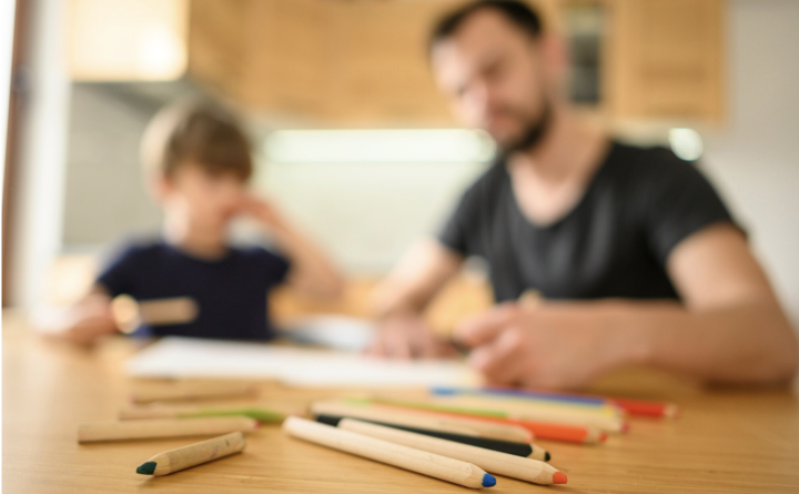 Vater und Junge sitzen am Kuechentisch und machen zusammen Schulaufgaben.