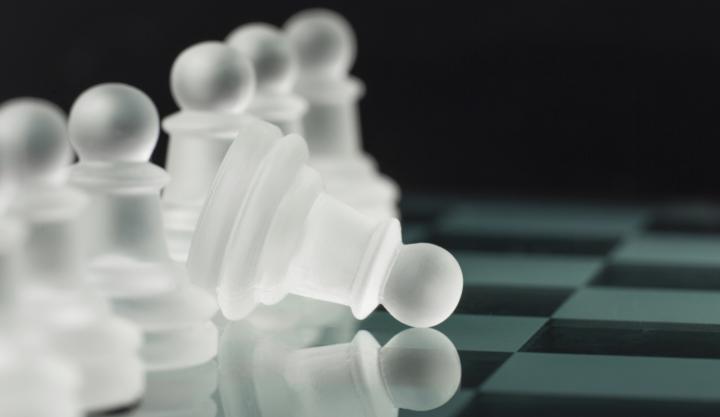 Stilisiertes Schachbrett mit einer Reihe Bauern, ein Bauer ist aufs Spielbrett gekippt.