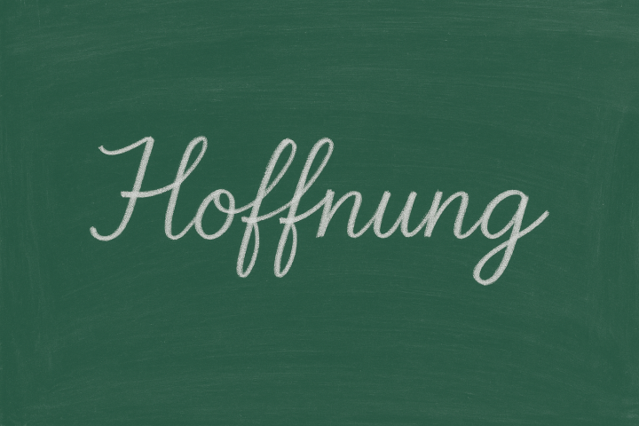 Schultafel, auf der in Schreibschrift mit weisse rKreide das Wort Hoffnung steht.