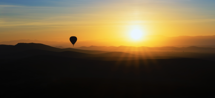 Sonnenaufgang über Hügeln mit Heissluftballon.