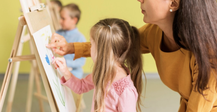 Erzieherin hilft Kind an der Staffelei beim Malen von Blumen.