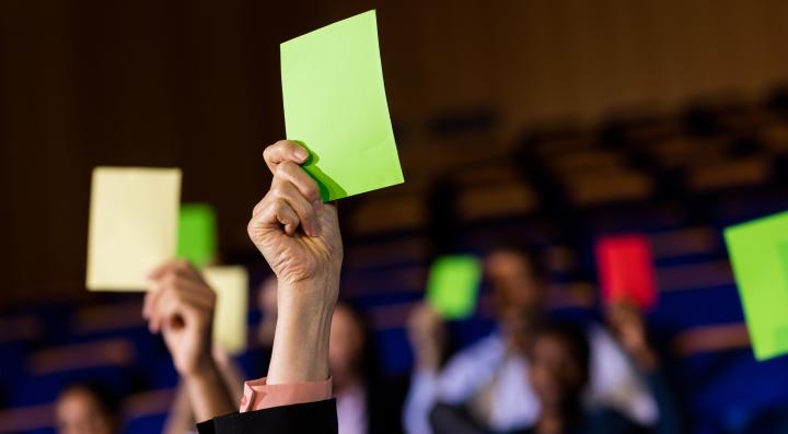 In die Luft gereckte Haende mit gruenen und einer roten Abstimmungskarte.