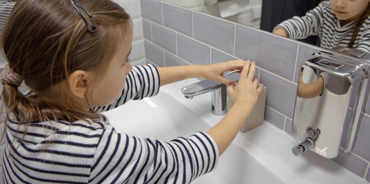 Schuelerin pumpt Seife aus Spender, um Haende zu waschen.
