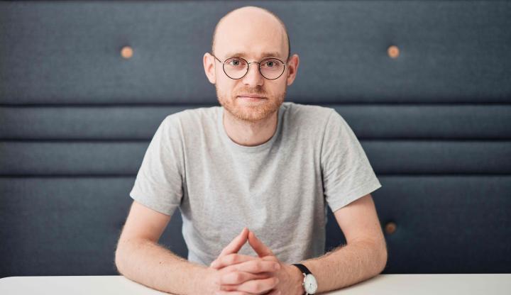 Portraitfoto David Alders, an einem Tisch sitzend, mit dunkelgrauem Hintergrund.