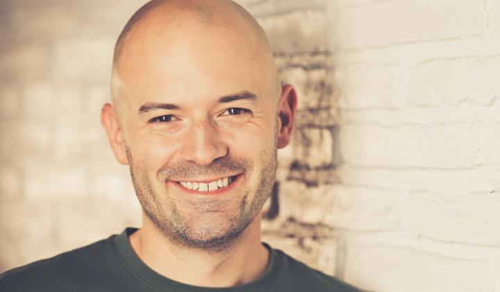 Portraitfoto Dennis Meistereck vor heller Backsteinmauer.
