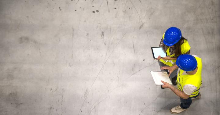 Zwei Arbeiter mit blauen Helmen und gelben Warnwesten auf einer Betonfläche aus der Vogelperspektive.