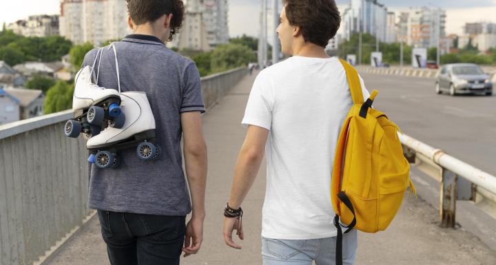 Zwei Freunde verbringen draussen Zeit zusammen, einer mit Rucksack, der andere mit Rollschuhen.
