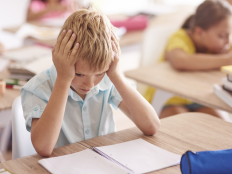 Grundschueler im Klassenraum, Kopf in die Haende gestuetzt.