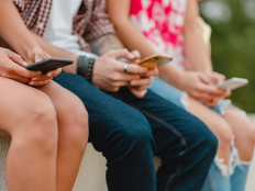 Jugendliche sitzen auf einer Mauer und nutzen ihre Handys.