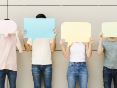 Eine Gruppe von vier jungen Menschen hält sich leere Sprechblasen vor das Gesicht.