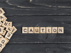 Scrabble-Spielsteine bilden das englische Wort "Caution" auf schwarzem Holz.