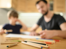 Vater und Junge sitzen am Kuechentisch und machen zusammen Schulaufgaben.