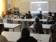 Klassenzimmer mit Schuelerinnen und Schuelern, vorn an der Tafel "Arabboy"-Autorin Güner Yasemin Balci.