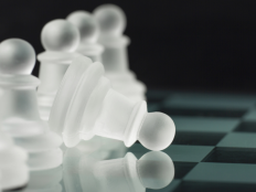 Stilisiertes Schachbrett mit einer Reihe Bauern, ein Bauer ist aufs Spielbrett gekippt.