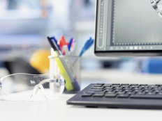 Ausschnitt eines Schreibtischs mit Schutzbrille, Stiftbecher und Computer.