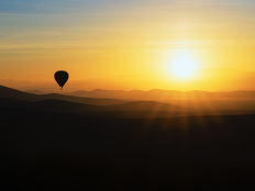 Sonnenaufgang über Hügeln mit Heissluftballon.
