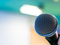 Close-Up eines schwarzen Mikrofons vor verschwommenem Hintergrund.