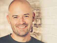 Portraitfoto Dennis Meistereck vor heller Backsteinmauer.