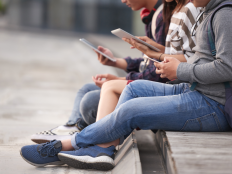 Jugendliche sitzen draussen nebeneinander und nutzen ihre Smartphones.