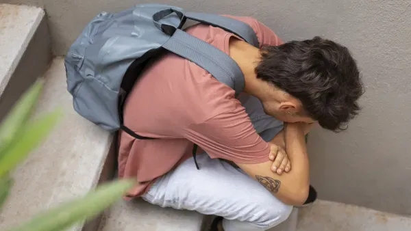 Schueler mit Rucksack sitzt auf einer Treppe, Kopf auf die Haende gestuetzt.