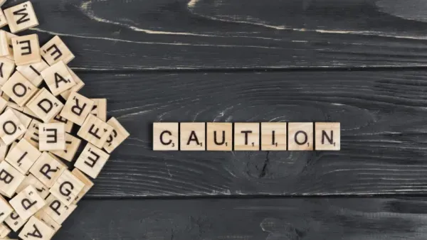 Scrabble-Spielsteine bilden das englische Wort "Caution" auf schwarzem Holz.