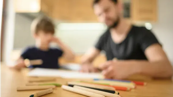 Vater und Junge sitzen am Kuechentisch und machen zusammen Schulaufgaben.