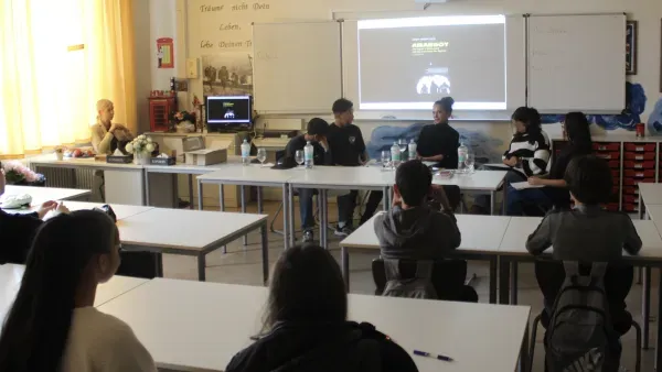 Klassenzimmer mit Schuelerinnen und Schuelern, vorn an der Tafel "Arabboy"-Autorin Güner Yasemin Balci.