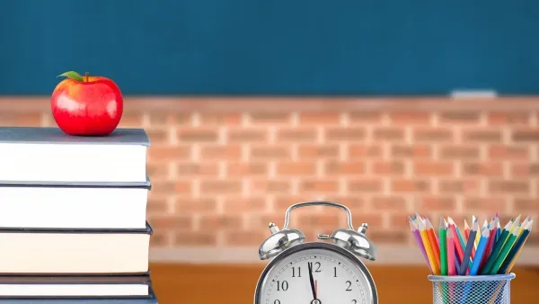 Stilleben Lehrerschreibtisch mit Buechern, Apfel, Wecker und Becher mit Buntstiften.