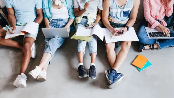 Gruppe junger Menschen auf dem Boden sitzend mit Buechern, Heften, Laptops und Smartphones.