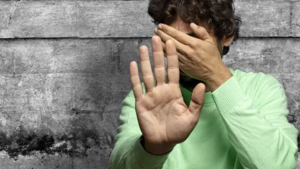 Nahaufnahme eines Jugendlichen vor grauer Wand, der sich schuetzend die Hand vors Gesicht haelt.