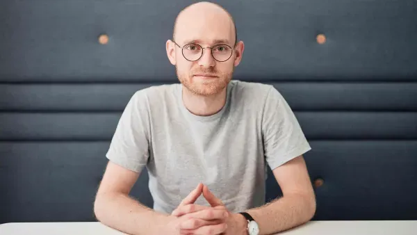 Portraitfoto David Alders, an einem Tisch sitzend, mit dunkelgrauem Hintergrund.