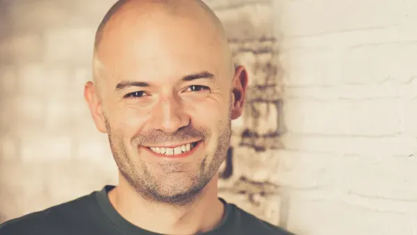 Portraitfoto Dennis Meistereck vor heller Backsteinmauer.