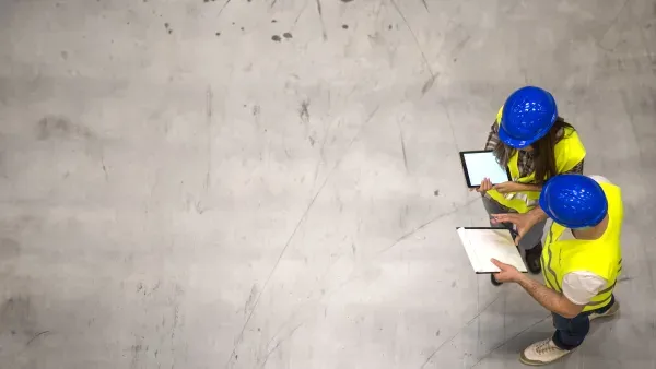 Zwei Arbeiter mit blauen Helmen und gelben Warnwesten auf einer Betonfläche aus der Vogelperspektive.