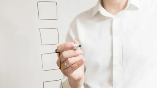 Check-Boxen auf transparentem Glas vor einer Geschäftsperson mit Stift in der Hand.